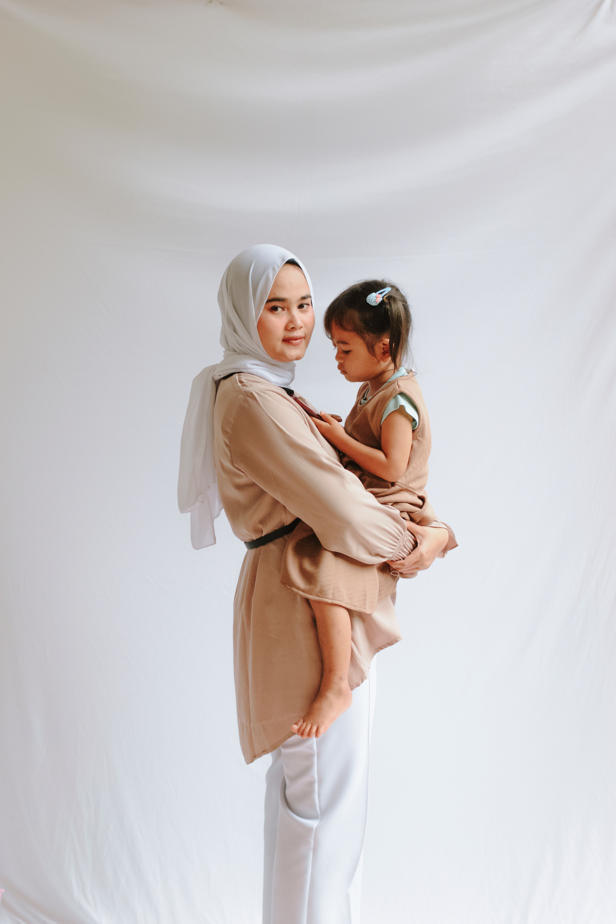 Mother in Hijab Carrying Her Daughter in Brown Dress